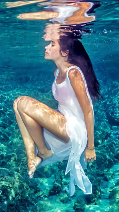 Mujer en posicion casi fetal sumergida en las aguas del mar muerto con un vestido blanco